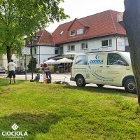 Zwei Glasfaser-Monteure der CIOCIOLA Gruppe spleißen Glasfasern auf einer grünen Wiese direkt an einer Straße.